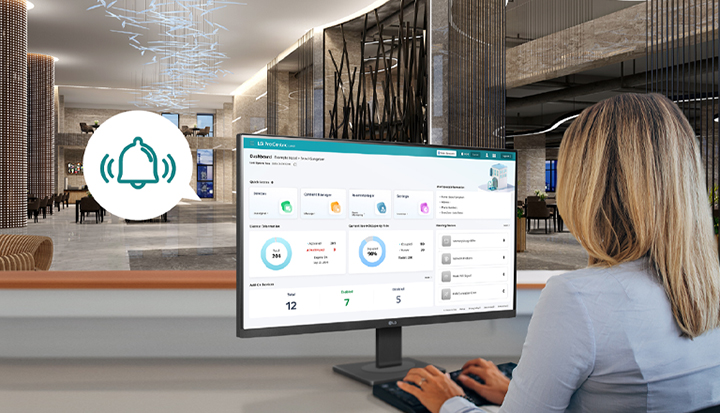 The image shows a hotel staff member monitoring the dashboard screen provided by LG Pro:Centric Cloud.
